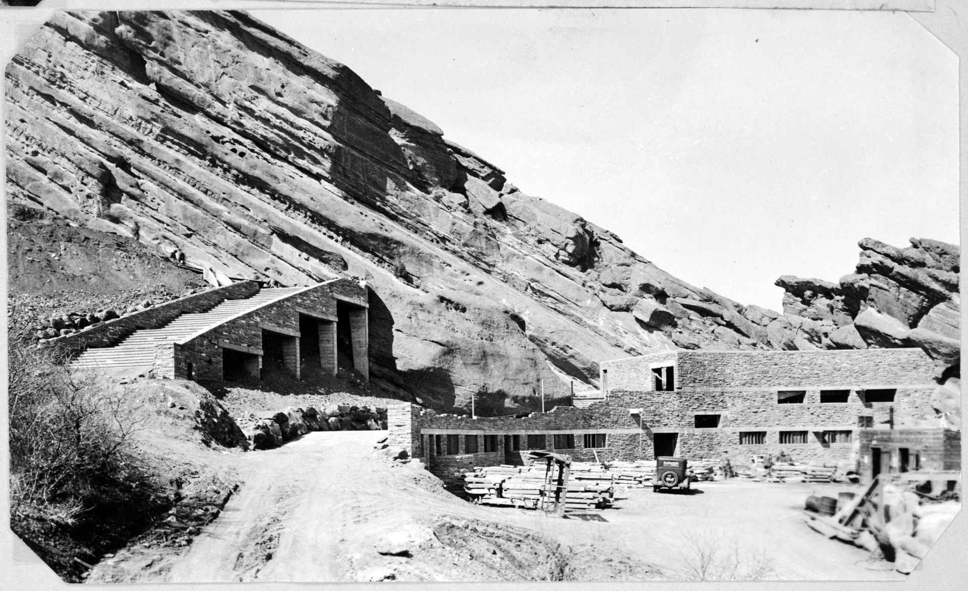 Black-and-white photograph showing the construction of Red Rocks Amphitheatre, with partially completed stone structures and stairs set against large rock formations.